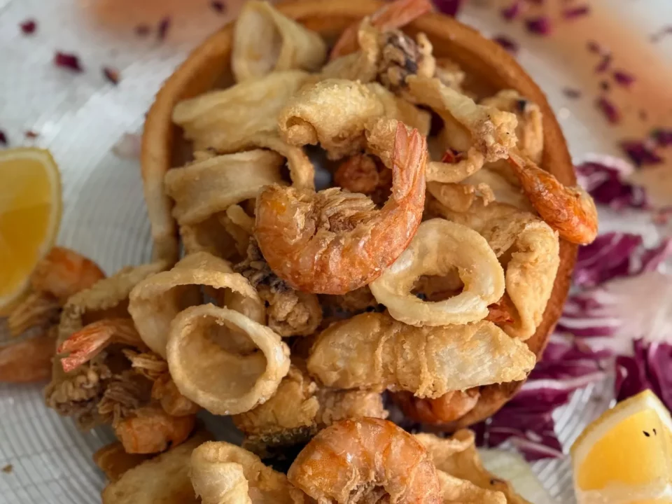 Frittura di calamari e gamberi servita su piatto elegante con limone e radicchio al Ristorante Pizzeria Il Piacere di Modena, specializzato in cucina di pesce